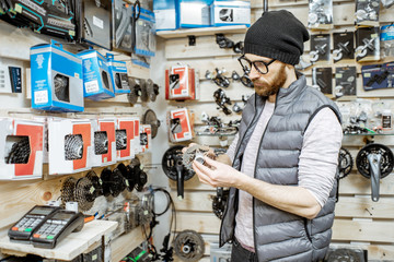 Stylish man choosing gear stars, buying bicycle parts at the small bicycle shop