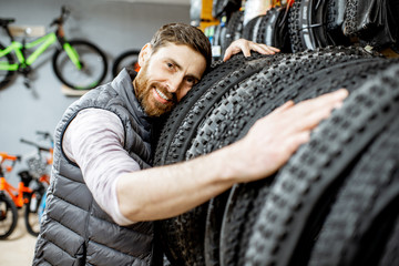 Portrait of a man as a salesman or customer hugging new bicycle tires at the bicycle shop