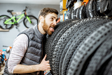 Funny portrait of a man as a salesman or customer biting a new bicycle tire at the bicycle shop