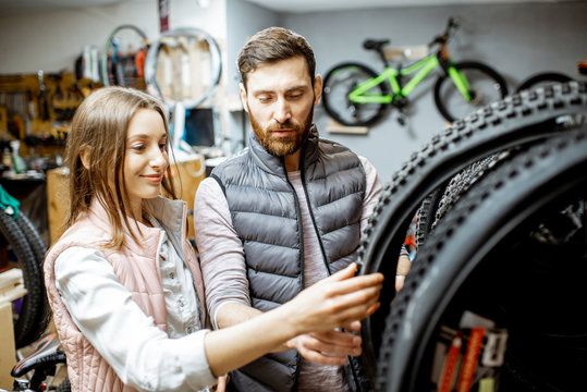 Salesman Helping Young Woman To Choose A New Bicycle Tire In The Sports Shop