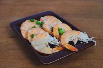 Steamed white shrimp in dish on wood background.