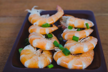 Steamed white shrimp in dish on wood background.