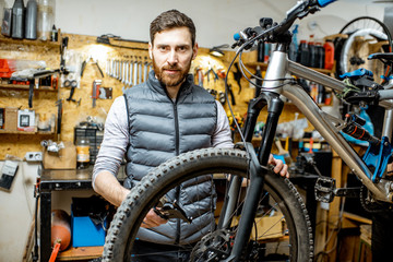 Fototapeta na wymiar Portrait of a handsome repairman standing in the bicycle workshop with working tools on the background