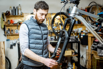 Fototapeta na wymiar Handsome repairman serving a bicycle, fixing some malfunctions with bicycle fork at the workroom