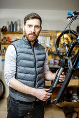 Portrait of a handsome repairman serving a bicycle, fixing some malfunctions with bicycle fork at the workroom