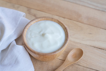 Natural homemade plain organic yogurt in wooden bowl and wood spoon on wood texture background