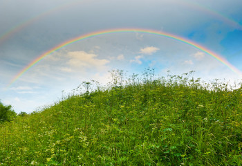 Naklejka premium Bright rainbow in the sky with clouds above the hill