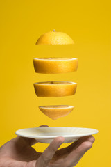 Flying lemon slices over a white saucer. Yellow background.