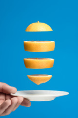 Flying lemon slices over a white saucer. Blue background.
