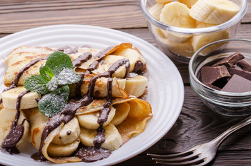 French crepes with chocolate sauce and banana in ceramic dish on wooden kitchen table