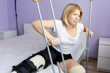 Sad woman after an operation on her leg is sitting on the bed.