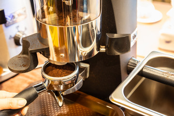 Close up woman hand holding portafilter, girl barista is grinding the roasted coffee beans into powder using coffee grinder at cafe shop