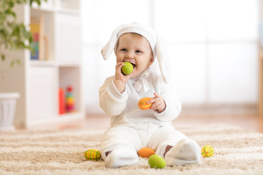 Cute little baby in white bunny costume sits on rug at home