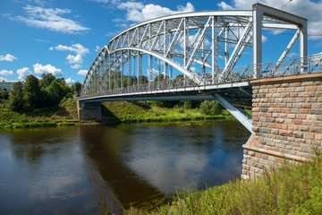 First in Russia steel arch bridge on river Msta in sunny summer day. Novgorod region, Borovichi, Russia. Was built in 1905.