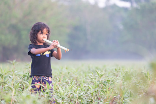 The little girl is blowing the flute in the middle of the grassland in the morning.