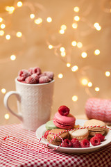Obraz na płótnie Canvas Birthday surprise: french dessert macaroons served on a white plate with fresh raspberries and a mug of fruit smoothie. Background decorated with lights