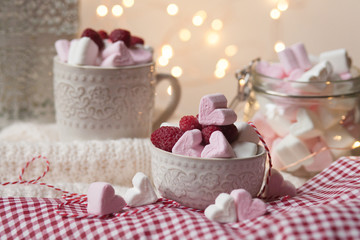 Home saint valentine's day party: heart shaped white and pink marshmallow served with fresh raspberry. Table decorated with red tablecloth and white knitted rud and lights