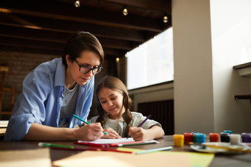 Portrait of modern young woman with daughter drawing together at home, copy space