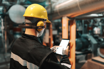 Caucasian worker in heavy industry plant with helmet and in uniform using tablet for work.