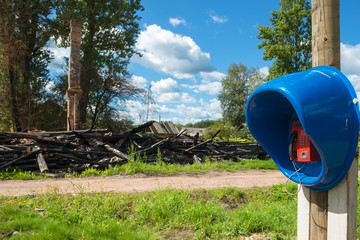 Payphone in the village opposite a burnt wooden house