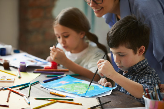 Portrait of two little kids, girl and boy painting pictures with loving mother, copy space