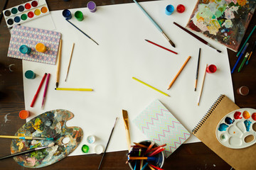 Top view of art background with art supplies, paints and brushes over white paper, copy space