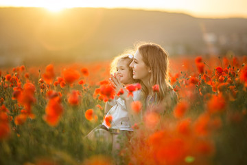 Beautiful smiling baby girl with mother are having fun in field of red poppy flowers over sunset lights, spring time - obrazy, fototapety, plakaty