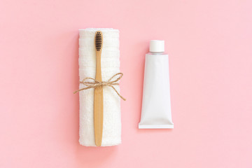 Fototapeta na wymiar Natural eco-friendly bamboo brush on white towel and toothpaste tube. Set for washing on paper pink background. Close up, Copy space for text or your design Top view Flat lay