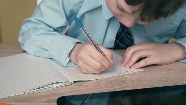 Ext CU, Tracking: Schoolboy does homework, writes pen in notebook, on the table is tablet.