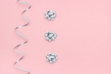 Silver streamers serpentine and bows on pink background in minimal style. Concept decorations for celebration, party, holiday, Christmas, birthday, new year