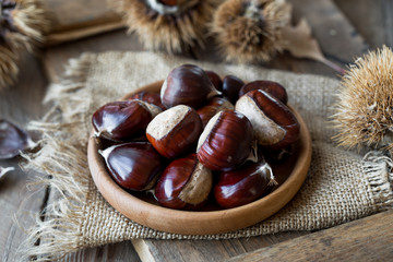 Roasted chestnuts in cast iron grilling pan over rustic wooden board  background, 