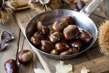 Roasted chestnuts in cast iron grilling pan over rustic wooden board  background, 