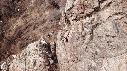 Climbers climb the rock. Drone footage. Side and top view. Rock lesson in the highlands. Gray rocks and dry bushes. Sometimes there is snow. Steep rock and cracks in places.