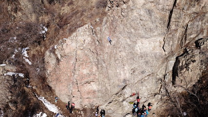 Climbers climb the rock. Drone footage. Side and top view. Rock lesson in the highlands. Gray rocks and dry bushes. Sometimes there is snow. Steep rock and cracks in places.