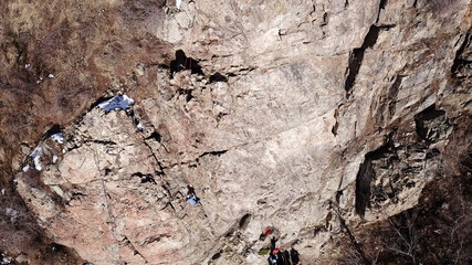 Climbers climb the rock. Drone footage. Side and top view. Rock lesson in the highlands. Gray rocks and dry bushes. Sometimes there is snow. Steep rock and cracks in places.