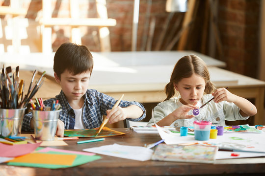 Portrait of two children boy and girl painting together sitting at table at home, copy space