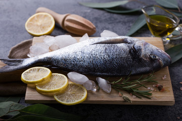 Mediterranean seafood concept. Raw dorado fish with olive oil, lemon, rosemary on stone table. Fresh organic sea bream or dorada fish. Top view dorado fish