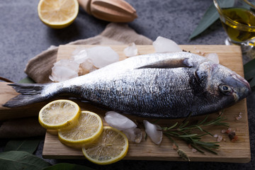 Mediterranean seafood concept. Raw dorado fish with olive oil, lemon, rosemary on stone table. Fresh organic sea bream or dorada fish. Top view dorado fish