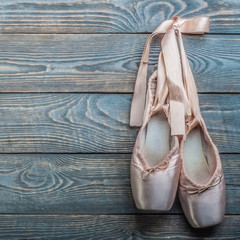 Pointe shoes ballet dance shoes with a bow of ribbons hang on a nail on a wooden background.