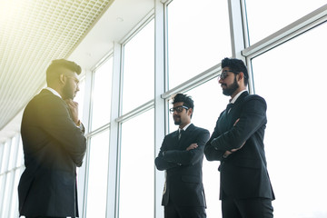 Three asian corporate executives standing in front of windows discussing business