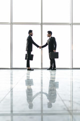 Fototapeta premium Full length side view of asian businessmen shaking hands in office building with panoramic glasses