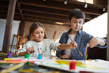 Portrait of two happy children, brother and sister painting picture together, copy space