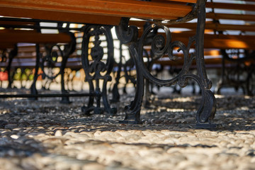 Fototapeta na wymiar Cast iron decorative bench with plastic inserts. Benches standing on a pebble in the summertime shade