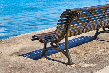 Naklejka na ściany i meble Single old-fashioned cast iron and wood park bench on a sunny day
