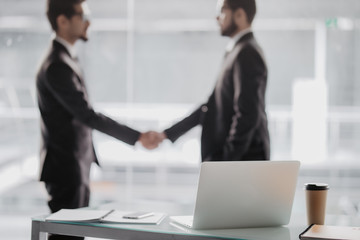 Two business people shaking hands in office as sign of partnership in office