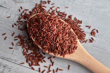 red rice on wooden spoon over wooden background
