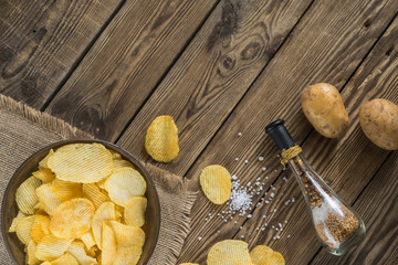 Potato chips in bowl on a wooden background, top view. Salty crisps scattered on a table.