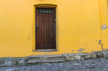 Bright colored wall with wooden door on the medieval streets of Sighisoara, Romania.