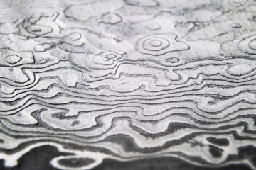 Background with pattern of damask steel. Close up. Macro shot of a damascus steel knife blade texture. Damascus steel pattern. Metal and steel background. Damascus steel with original pattern. © Aleksei