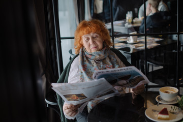 Old lady reading morning newspaper in cafe